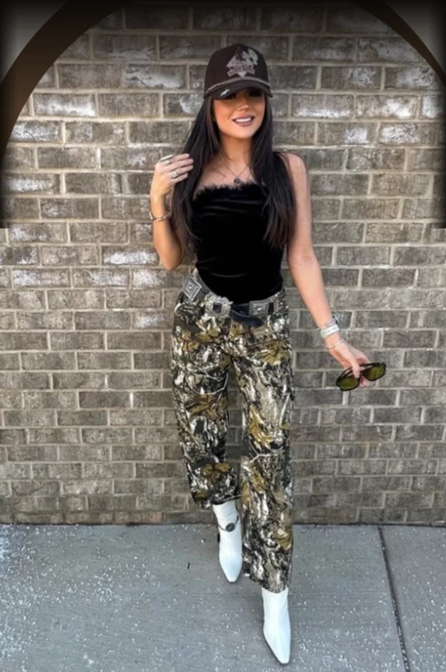 Maddy, founder of The Tipsy Boot, in a branded cap and white Western boots against a brick wall